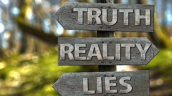Straßenschild das den Weg zur Wahrheit (rechts), Realität (links) und Lüge (rechts) weist.
