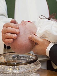 Ein Kleinkind wird über ein Taufbecken gehalten und getauft