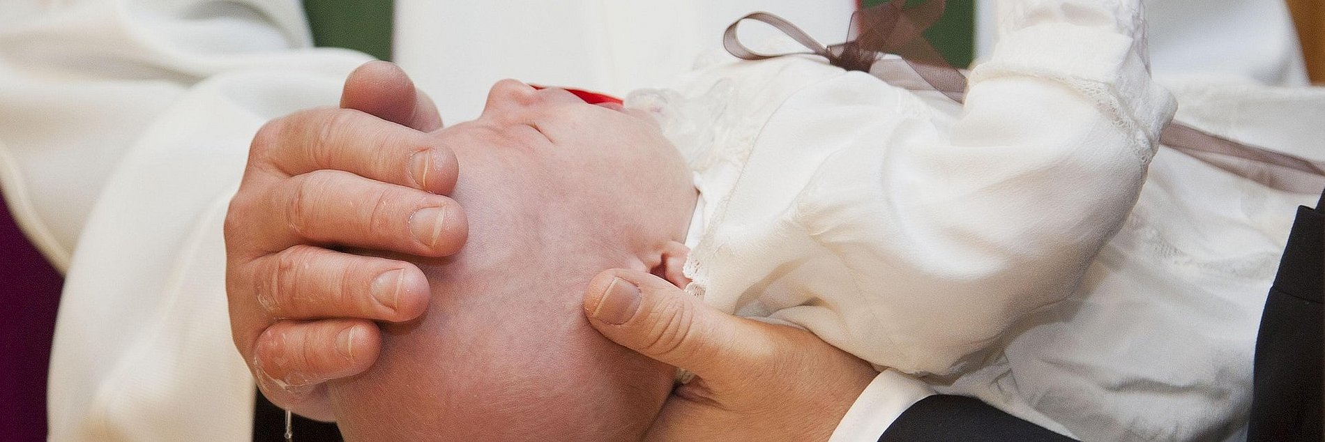 Ein Kleinkind wird über ein Taufbecken gehalten und getauft