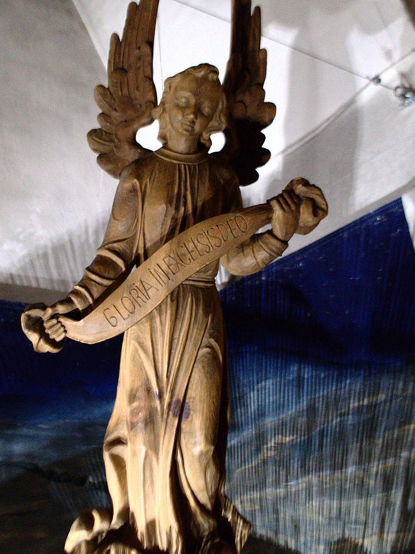 Detail aus der Krippenszene zeigt einen Engel aus Holz gefertigt, der über der Szenerie schwebt und ein Spruchband in Händen hält: Gloria in excelsis deo 