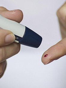 Mit einem Testgerät wird aus einem Bluttropfen auf einem Finger der Zuckerwert bestimmt