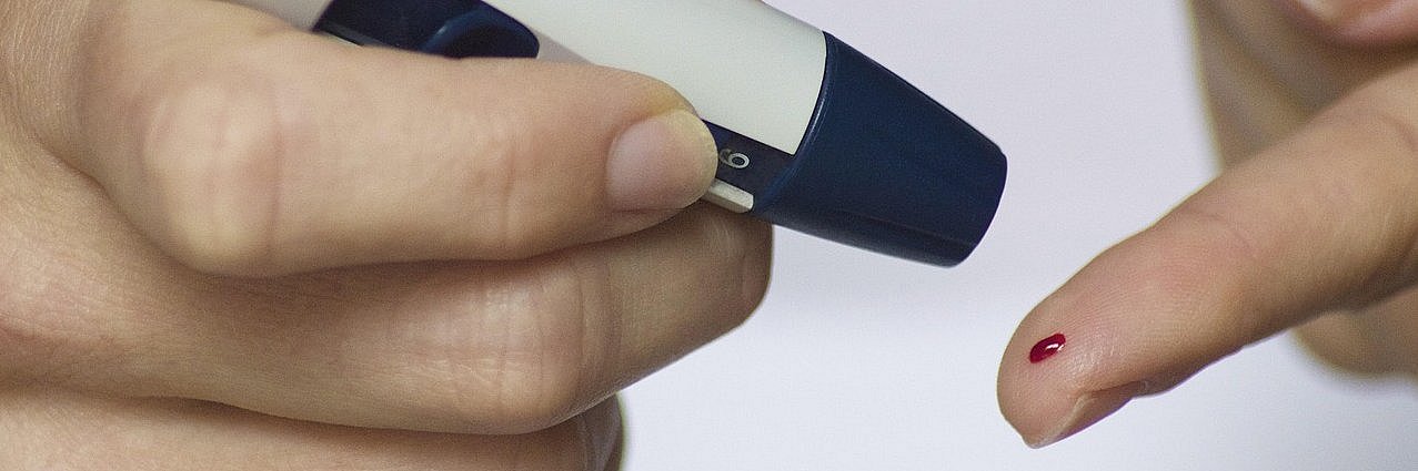 Mit einem Testgerät wird aus einem Bluttropfen auf einem Finger der Zuckerwert bestimmt