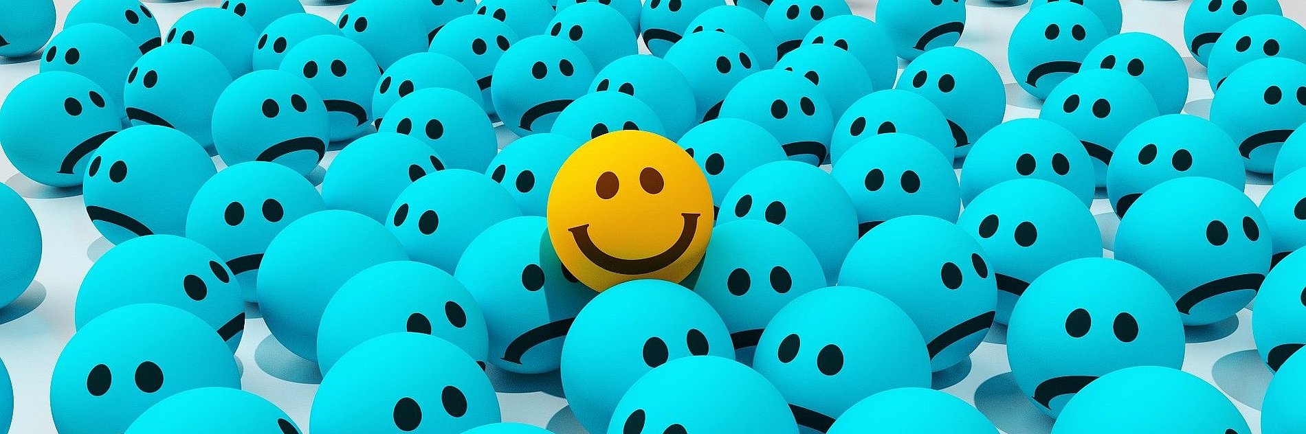 Ein sichtlich glücklicher gelber Smilie in einem Meer aus blauen schlecht gelaunten Smilies