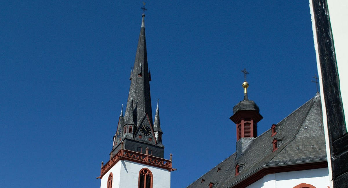 Die Kirche in Erbach mit weißer Fassade, roten Details und schwarz-grauem Schieferdach in der Grundform einer Basilika mit hohem Glockenturm